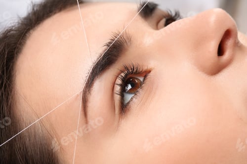 Preview: Young woman having professional eyebrow correction procedure, closeup