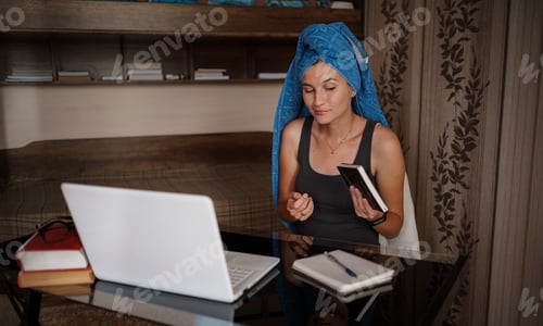 Preview: Woman with blue towel on head is working office work remotely from home. Using computer.