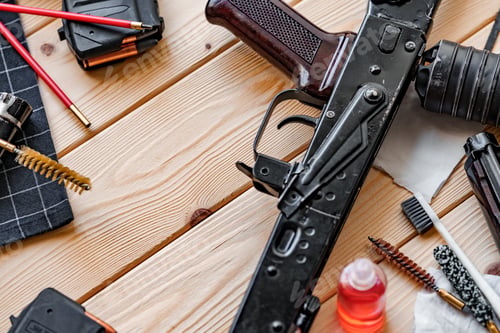 Preview: Black disassembled shotgun and cleaning tools on wooden table .