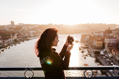 Preview: woman in Porto bridge taking pictures with camera at sunset. Tourism in city Europe. travel