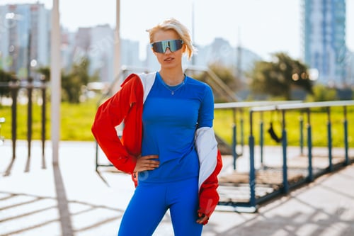 Vista previa: dynamic woman in sleek athletic gear poses confidently outdoors, with her red jacket draped