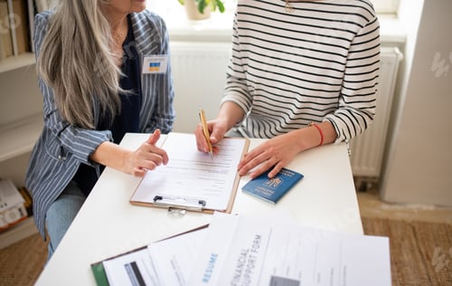 Preview: Senior woman volunteer helping Ukrainian woman to fill in forms at asylum centre.