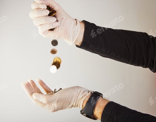 Preview: Hands of a man in white medical gloves pour money in the form of small coins