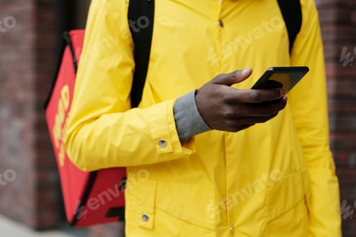 Preview: Close-up of young deliveryman from food service texting in smartphone