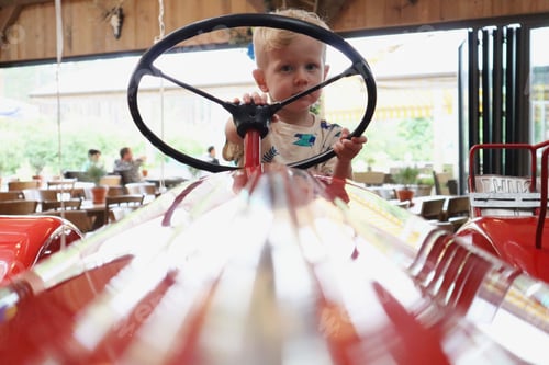 Preview: Little boy sitting behind the wheel of a red vintage tractor