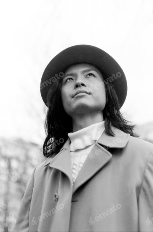 Preview: Young artist wearing hat and coat looking up in black and white analog photo