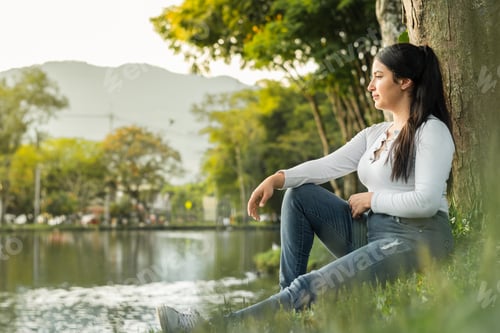 Preview: young latin woman sitting on the shore of a fishing lake, thinking and meditating about her future