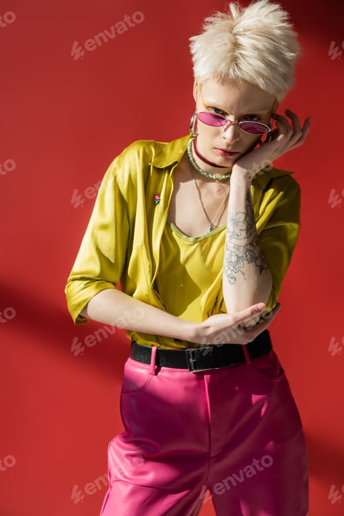Preview: sunlight on face of albino woman with tattoo posing in stylish sunglasses on carmine pink