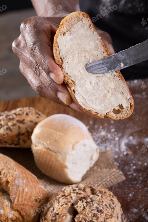 Preview: Cropped hands of african american male baker applying butter on bread slice