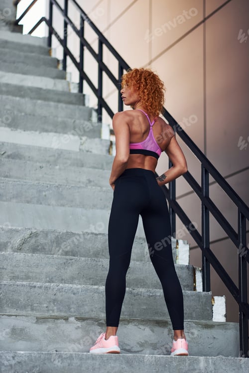 Preview: Young european redhead woman in sportive clothes showing her body and posing outdoors