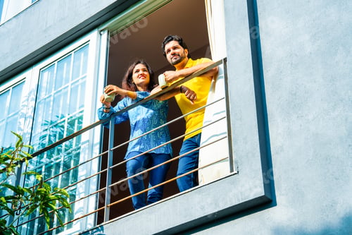 Preview: Indian couple in their thirties enjoying coffee and conversation on balcony in morning sun