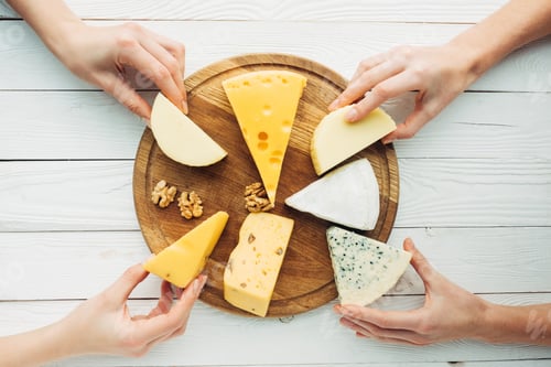 Preview: top view of female hands holding various types of cheese on wooden board