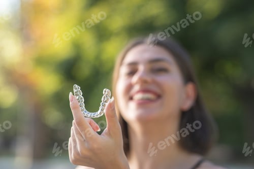 Preview: Beautiful smiling Turkish woman is holding an invisalign bracer