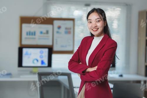 Preview: Professional woman in a red blazer standing confidently with arms crossed in a contemporary office e