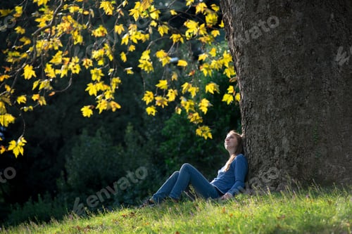 Preview: Girl sitting on the grass under a maple tree in autumn