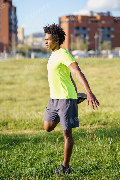 Preview: Black man stretching his quadriceps after running outdoors.