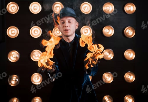 Preview: The fire is in his hands. Professional magician showing trick. Light bulbs on background