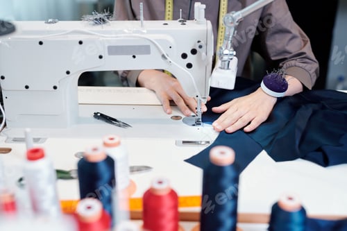 Preview: Female tailor hands moving piece of blue textile while sewing by machine