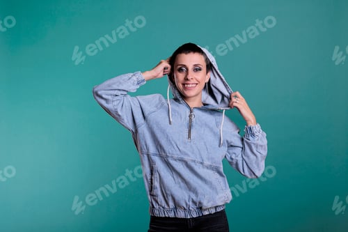 Preview: Smiling beautiful woman playing with hood while posing funny in studio