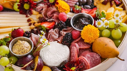 Preview: Cheese board served with fruits, nuts, ham, crackers, sweets. Plate of cheese and snacks on wooden b