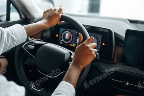 Preview: Two hands are on the steering wheel. Woman in white shirt is in the modern car