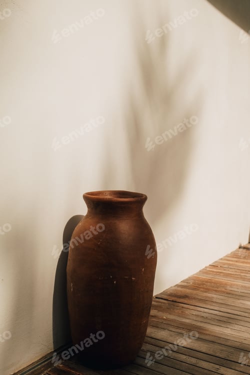 Preview: Rustic clay vase casting a shadow on a sunlit deck.