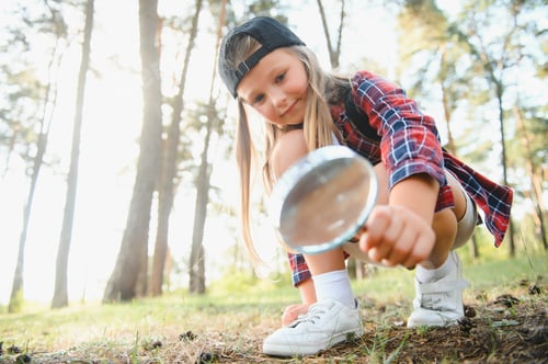 Preview: Rear view image of cute little girl exploring the nature with magnifying glass outdoor.