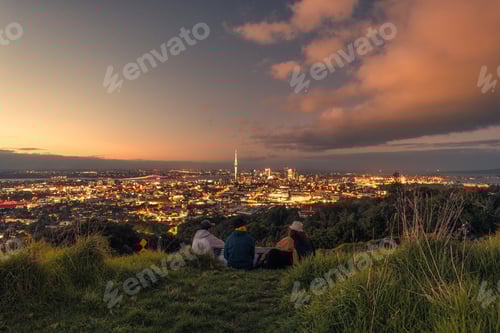 Preview: Group of tourist relaxing on Mount Eden with iconic sky tower during the sunset in Auckland