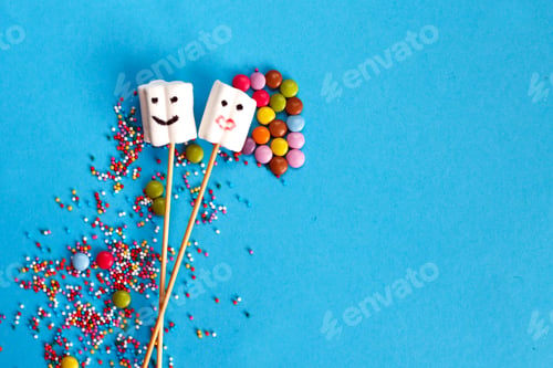 Preview: marshmallows on wooden skewers with color sweets on blue background.