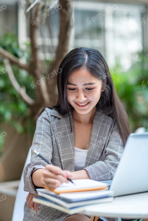 Preview: Beautiful Asian woman sitting taking notes at a coffee shop.