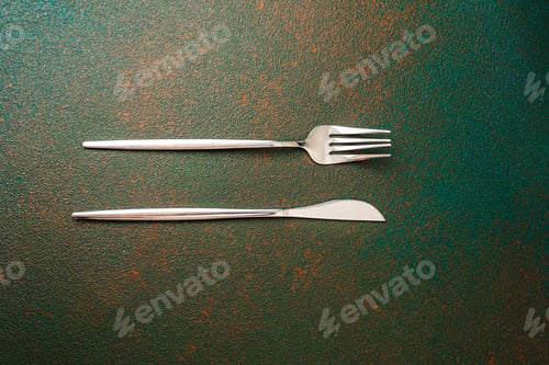 Preview: Silver fork and knife positioned on a textured green surface with rustic tones