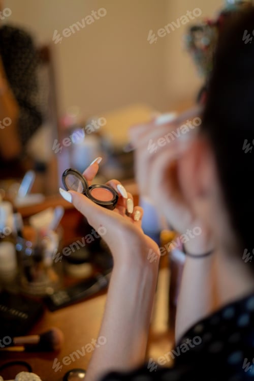 Preview: Young woman putting on make up in front of mirror