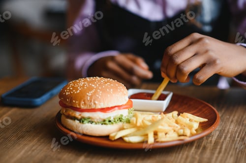 Preview: African girl eating burger and fries in cafe. Fast food concept