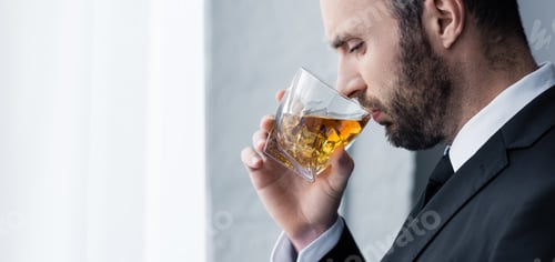 Preview: panoramic shot of sad, handsome bearded man drinking whiskey