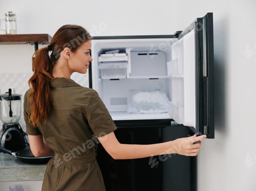 Preview: A woman smiling in the kitchen at home opened an empty freezer with ice inside, home refrigerator