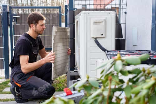 Preview: Technician servicing outdoor air source heat pump unit near house wall