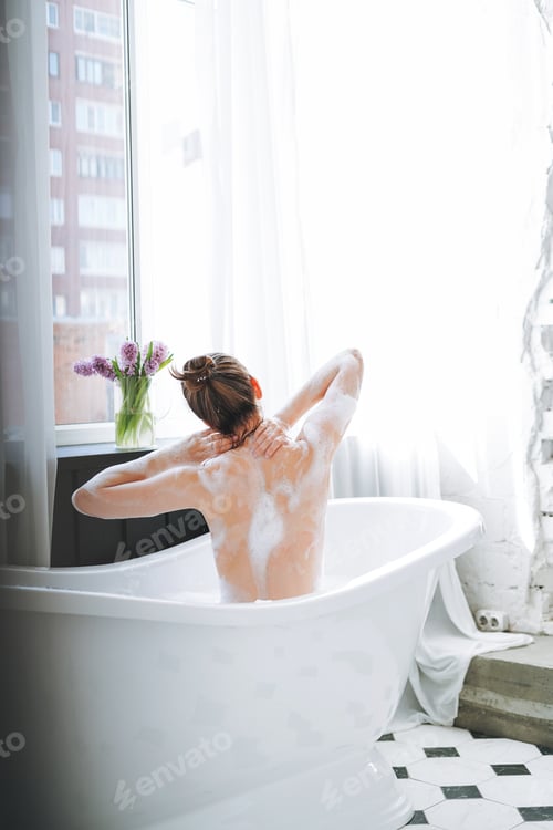 Preview: Young woman taking bath at home, treat yourself. People from behind