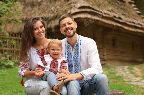 Preview: Happy family in Ukrainian national clothes sitting on bench outdoors