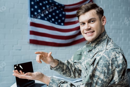 Preview: happy military man gesturing in office near laptop with blank screen