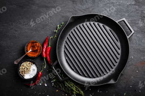 Preview: Empty cast-iron grill pan with ingredients for cooking on black background, top view