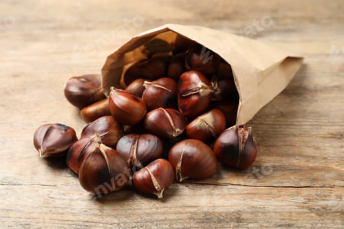 Preview: Delicious roasted edible chestnuts in paper bag on wooden table, closeup