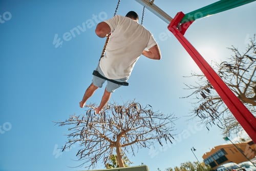 Preview: Man swinging on playground in sunlight