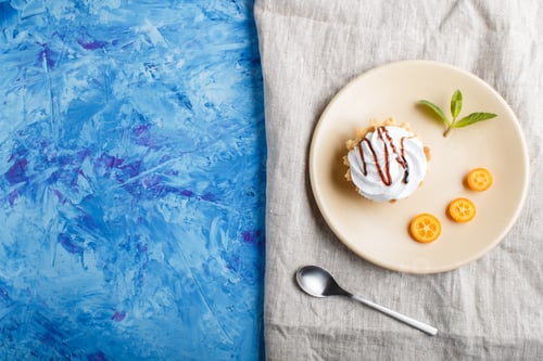 Preview: Cake with whipped egg cream on a light brown plate with kumquat slices and mint leaves