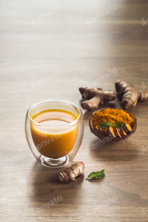 Preview: Organic orange turmeric drink, tea with cinnamon in a glass mug with fresh turmeric powder on wooden