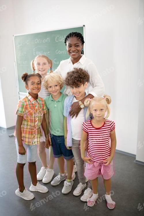 Visualização: Professora sorridente e amorosa abraçando seus lindos alunos inteligentes