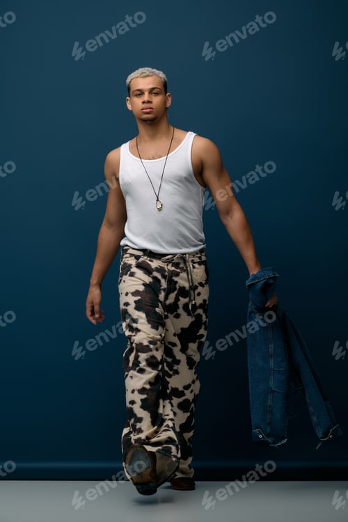 Preview: Stylish young man showcases fashion in denim jacket against a vibrant blue backdrop