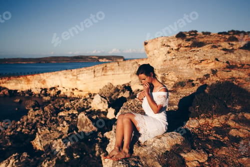 Woman in White Dress Seated near Ocean Cliffs