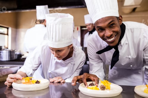 Preview: Male and female chefs garnishing delicious desserts in a plate