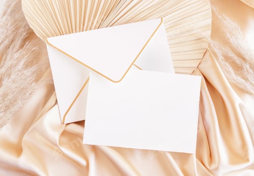 Preview: Blank card and envelope on beige satin fabric and dried palm leaf close up, romantic mockup