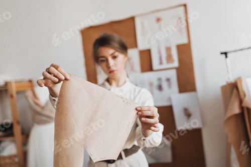 Preview: Lady in white blouse looks at paper shirt pattern. Brunette woman in beige pants and shirt designs